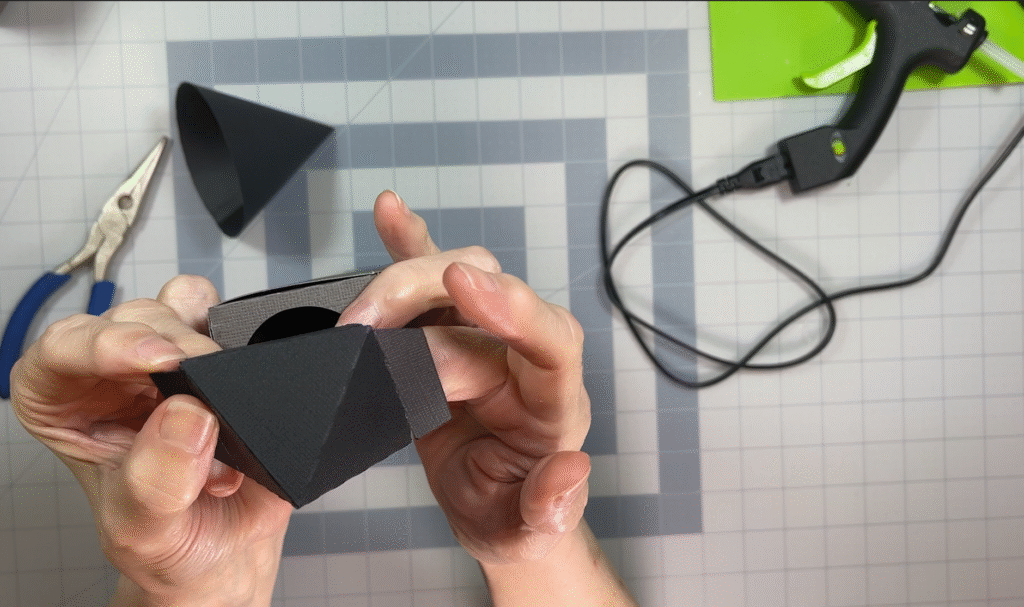 Hands attaching the roof piece to a 3D paper tower during the repair process.