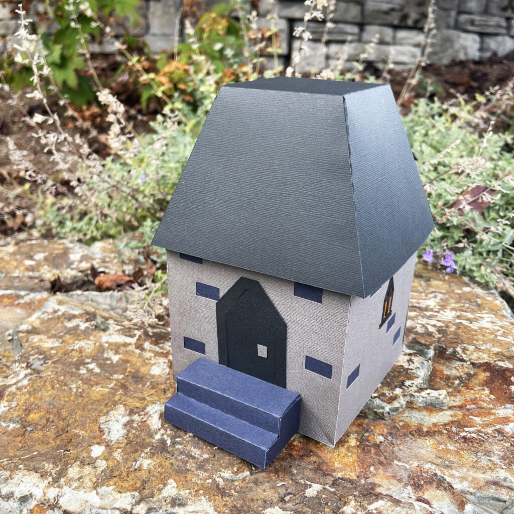 3D paper castle gatehouse with gray walls black roof and front steps displayed outdoors