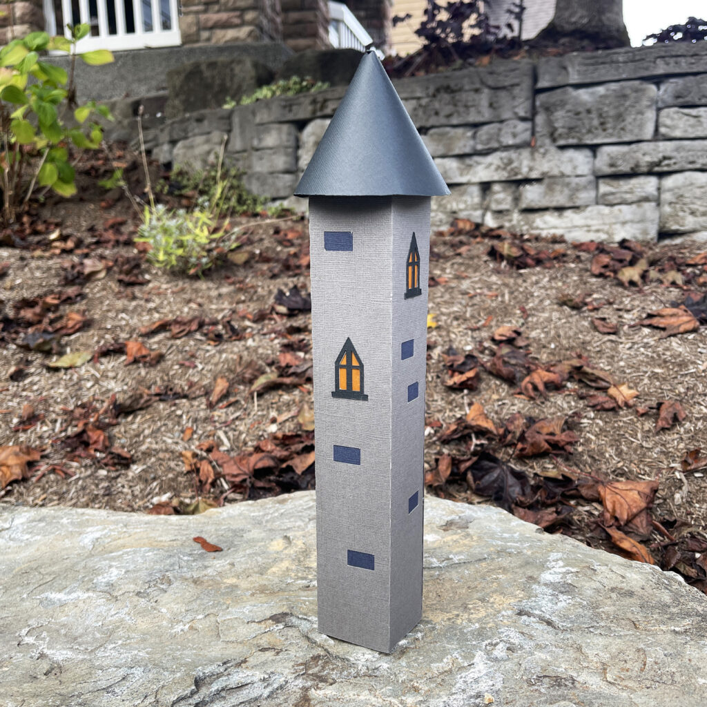 Tall 3D paper castle tower with gray stone texture and black pointed roof displayed outdoors