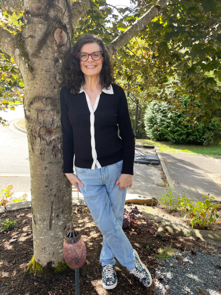 Portrait of Michelle Ward leaning against a tree, smiling warmly in natural light, dressed in a black sweater and jeans with colorful sneakers ‚Äî a bright, approachable creator moment.