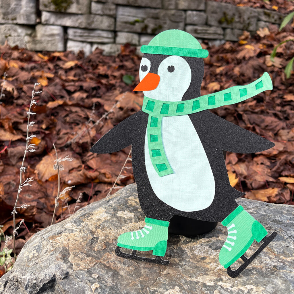 Paper penguin character named Finn Gladwell wearing a green hat scarf and ice skates displayed outdoors