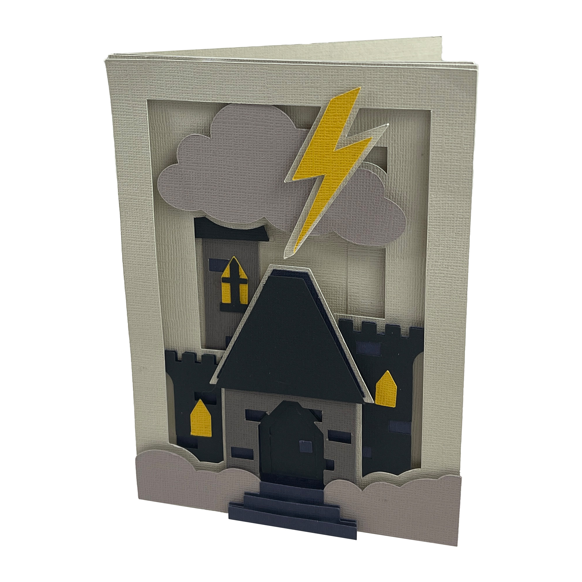 The finished Castle Shadow Box Card: a cream 5 by 7 card with a dark paper castle standing in a drift of fog, a gray storm cloud and a yellow lightning bolt above it, and warm yellow windows.