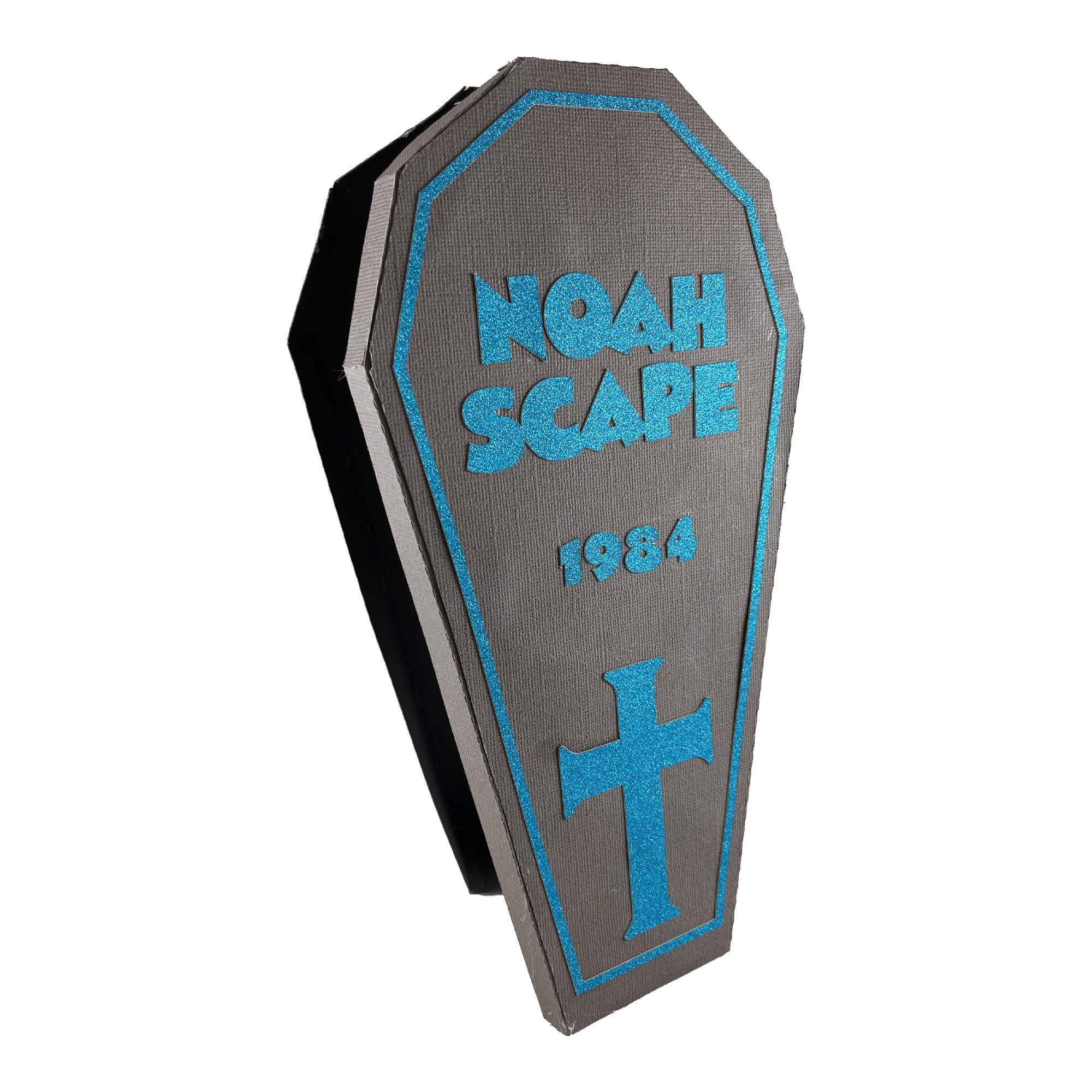 The finished Eight-Sided Coffin Box: a dark navy paper coffin with its lid on, lettered in blue vinyl with the name Noah Scape above a small cross.
